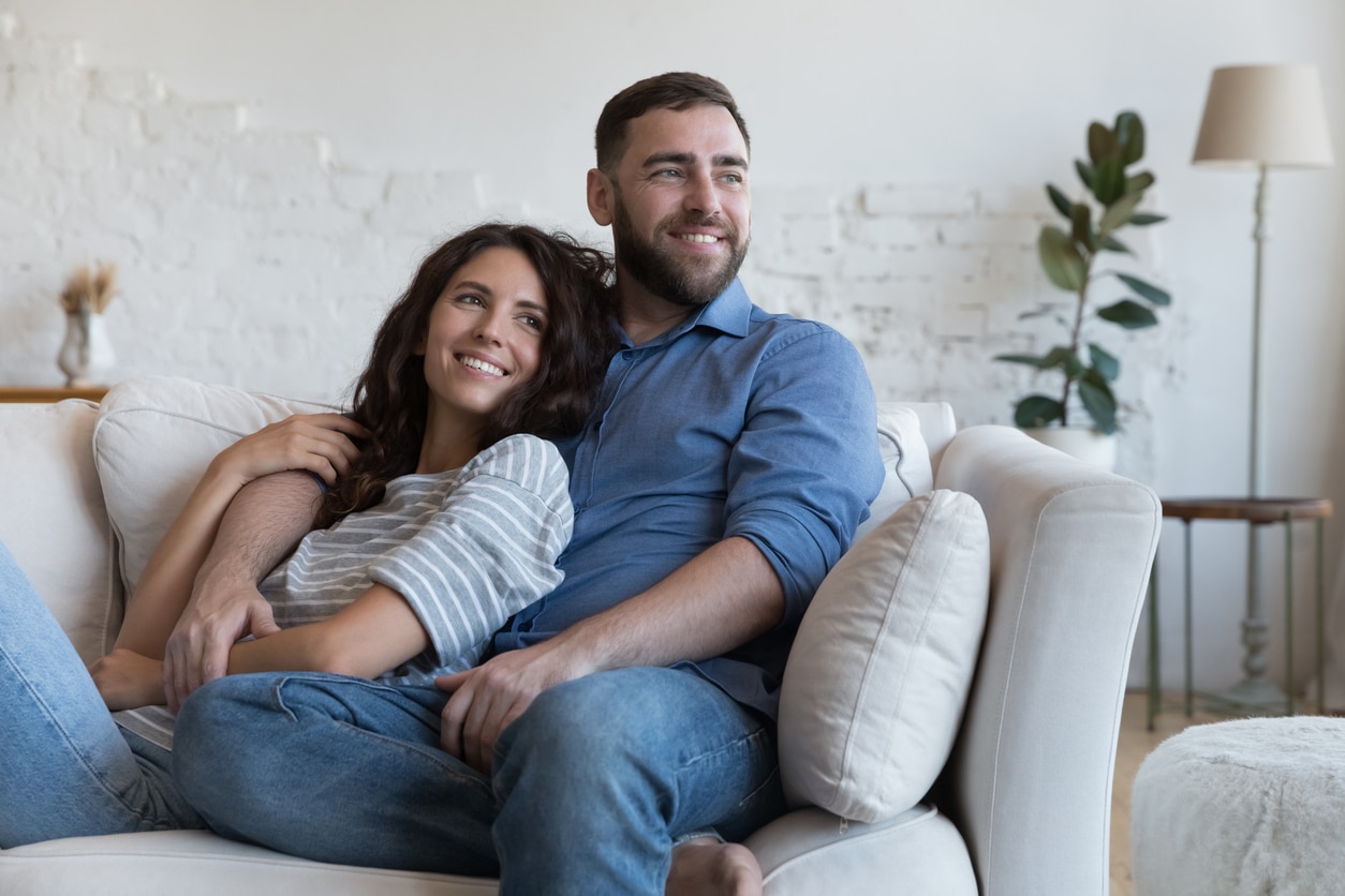 Cheerful dreamy young dating couple in love resting on sofa Cheerful dreamy young dating couple in love resting on sofa, relaxing at home, enjoying leisure, hugging, looking away, planning family future, marriage, mortgage, talking, laughing