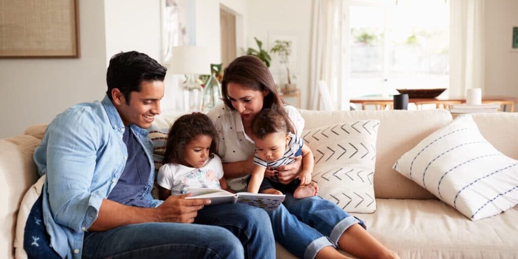 Hispanic,Couple,Sitting,On,The,Sofa,Reading,A,Book,At