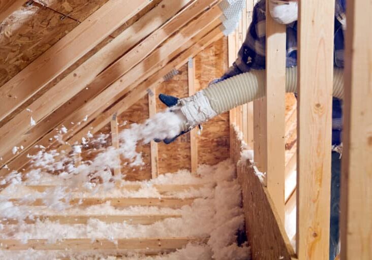 Worker Spraying Blown Fiberglass Insulation between Attic Trusses